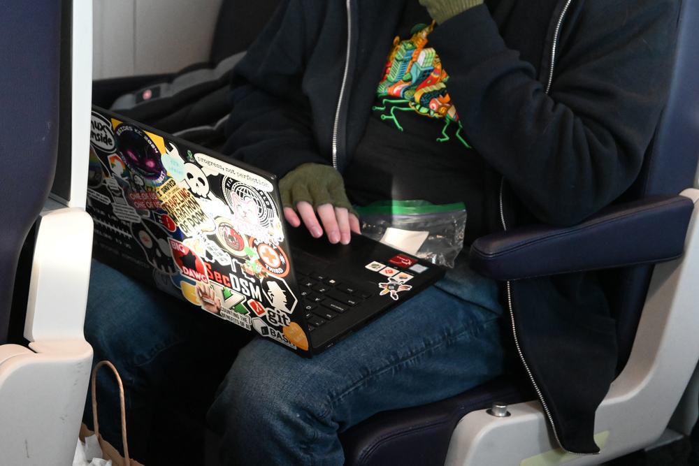 A sticker-covered laptop open on someone’s lap in an Amtrak seat