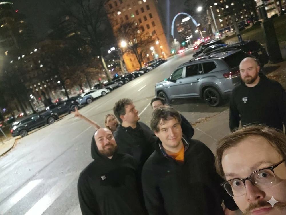 Group selfie of the Hobocon crew on a St. Louis street at night with the lit Gateway Arch in the distance