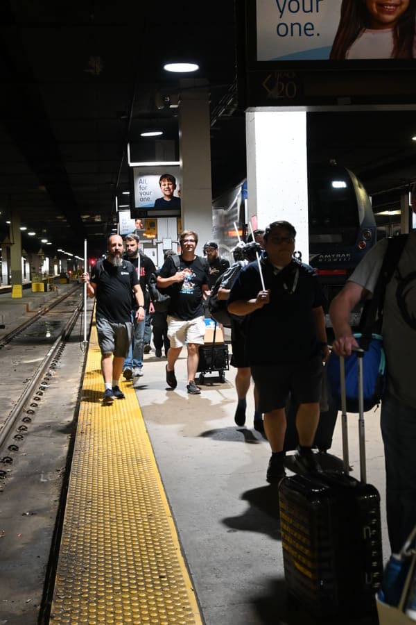 Attendees walking up a dim Chicago Union Station platform with luggage and gear, an Amtrak Midwest trainset alongside and a Track 20 sign overhead