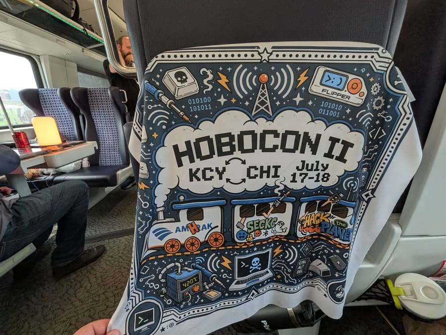 A Hobocon II bandana draped over a train seat back, illustrated with a steam train and hacking motifs and reading KCY to CHI, July 17-18