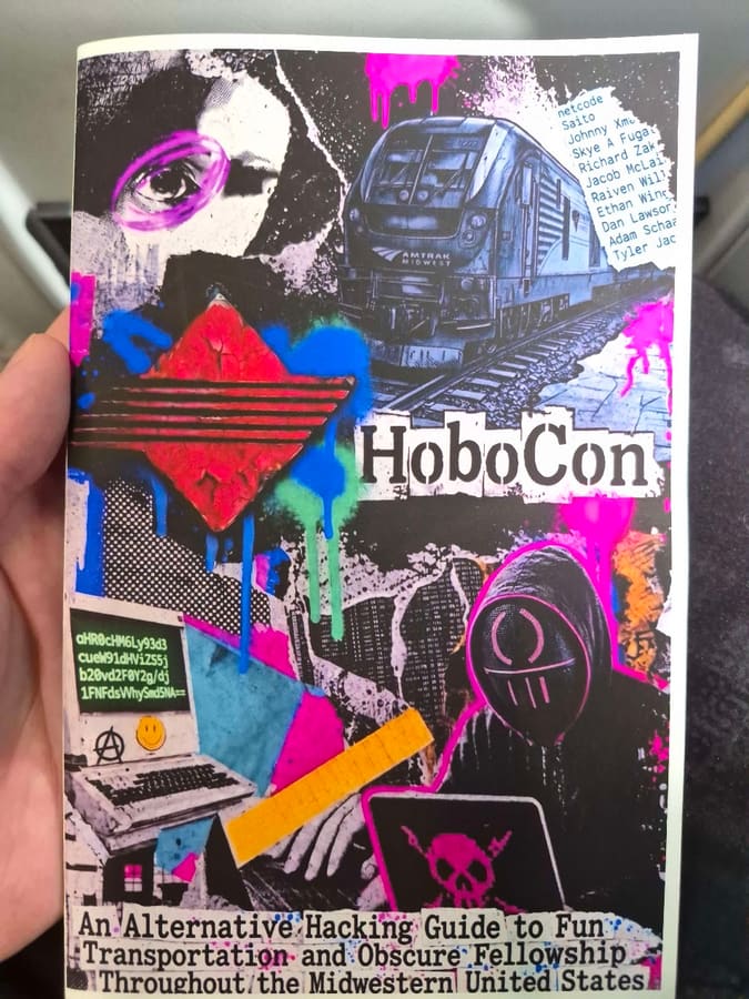 A hand holding the printed HoboCon zine, a neon collage cover with an Amtrak Midwest locomotive, a hooded figure, and cut-out lettering reading HoboCon